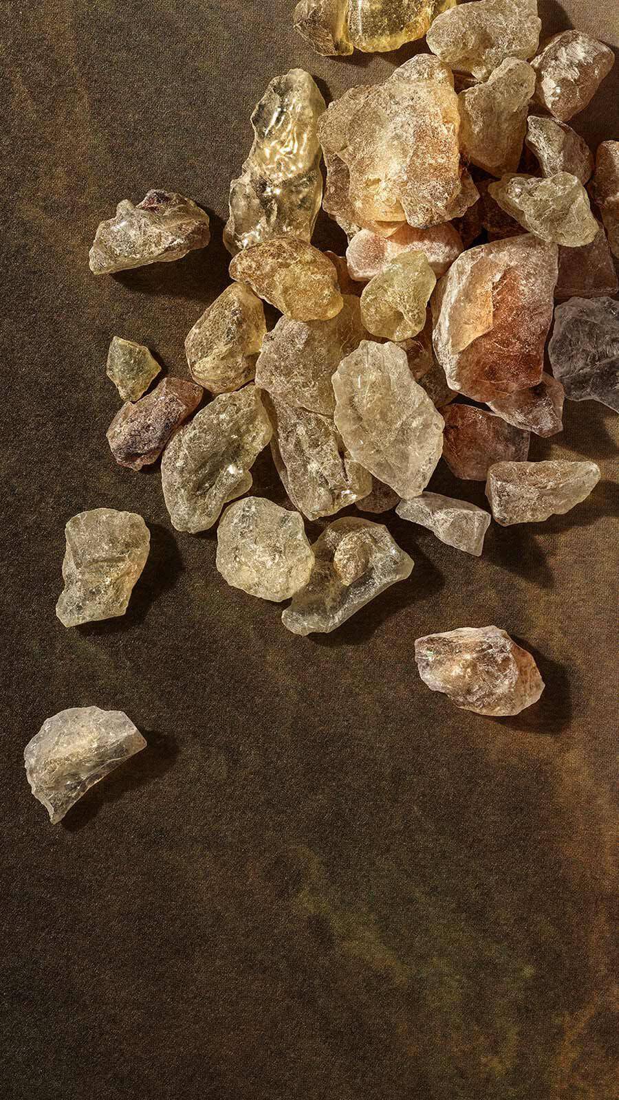 Pale golden frankincense resin crystals in a loose pile on a dark stone surface.